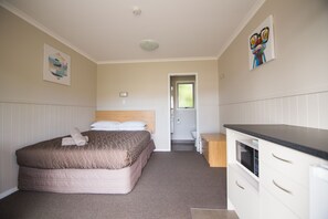 A bedroom with a bed, a bedside table, a microwave, and a door leading to a bathroom. - Stratford Motel & Holiday Park (Stratford)