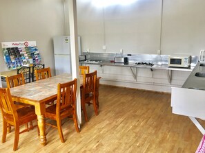 A dining area with a wooden table and chairs, a refrigerator, a microwave, and a gas stove in the kitchen area. - Stratford Motel & Holiday Park (Stratford)