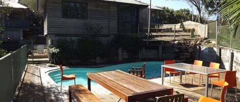 Une terrasse en bois avec une piscine, un espace salon extérieur et une maison en arrière-plan.