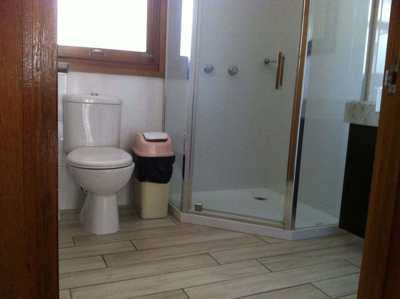 A bathroom with a toilet, a trash bin, and a glass-enclosed shower area.