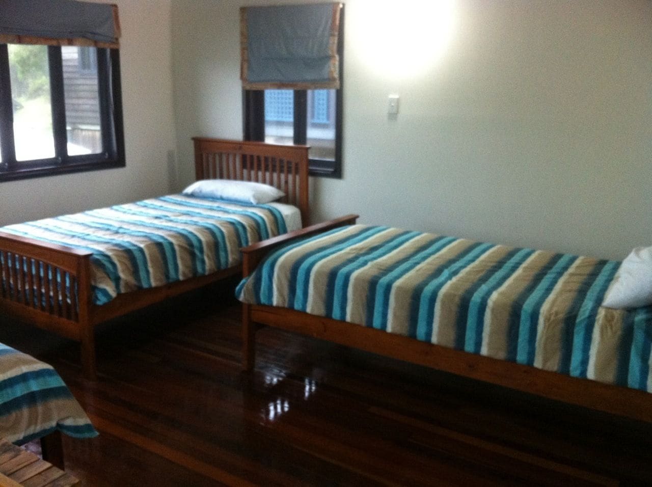 A room with two wooden beds with striped bedding, a window with a view, and a wall-mounted light fixture.