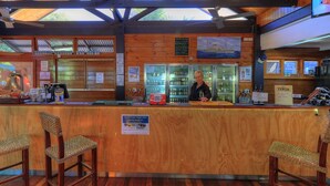 A wooden bar area with a counter, two wicker chairs, a refrigerator, and a sign reading "YENDA". - Fraser Island Retreat (K'gari (Fraser Island))