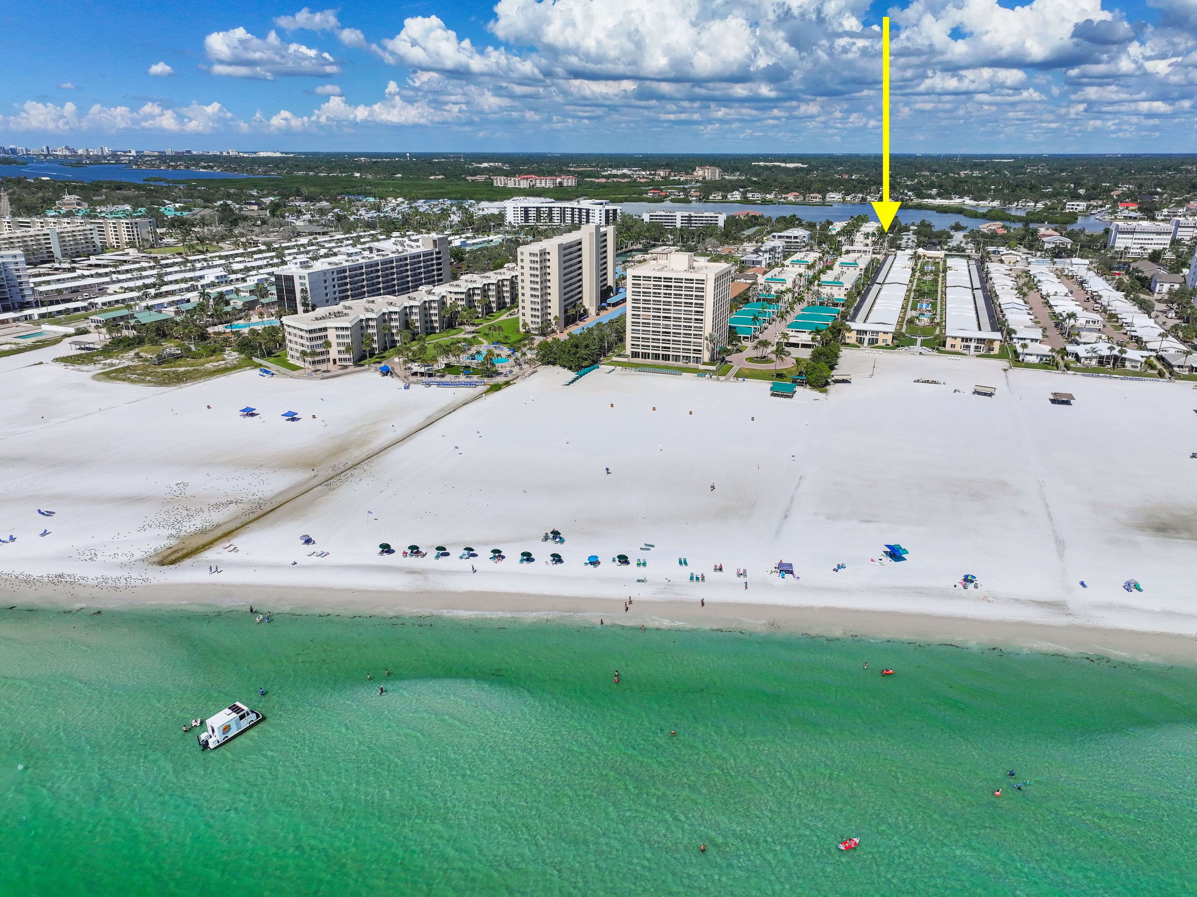 An aerial view of a coastal resort area with beachfront properties, a marina, and a clear view of the ocean.