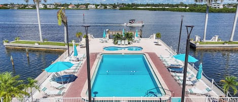 Ein rechteckiger Swimmingpool mit einer umlaufenden Liegefläche, Liegestühlen und Sonnenschirmen.