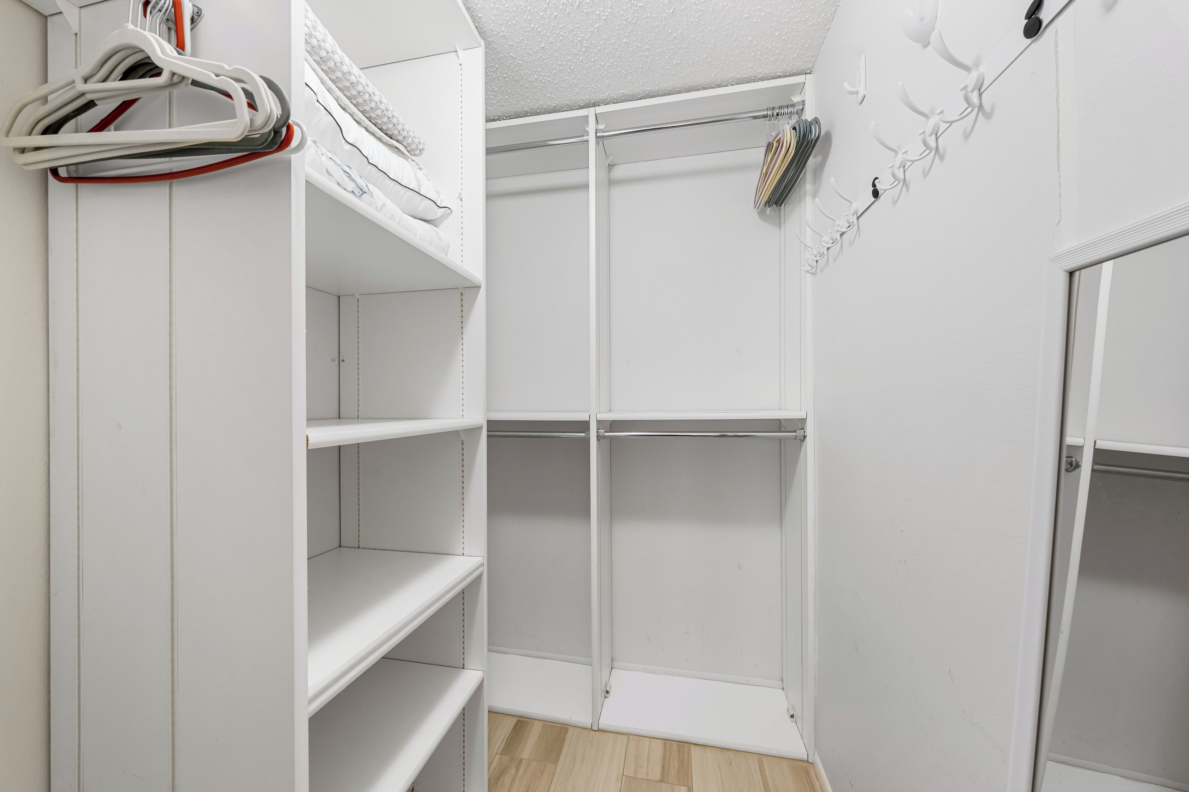 A white closet with open shelves and hanging space, a door with a handle, and a wall-mounted rack with hangers.