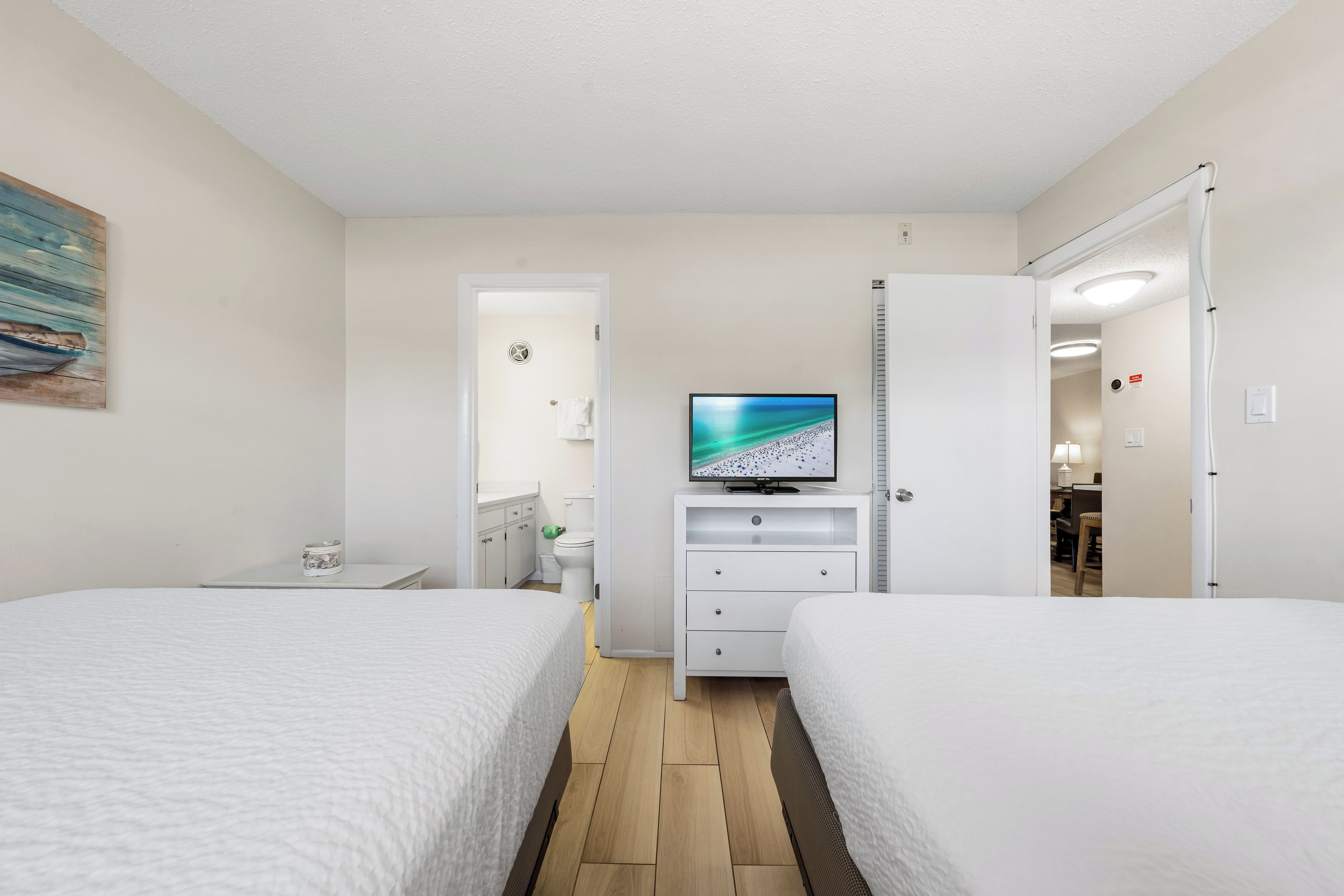 Ein Hotelzimmer mit zwei Betten, einem Fernseher, einem Schreibtisch und einem durch eine offene Tür einsehbaren Badezimmer.