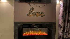 Una chimenea moderna con un televisor de pantalla plana montado encima, un letrero decorativo que dice 'love' y un fuego visible en su interior.