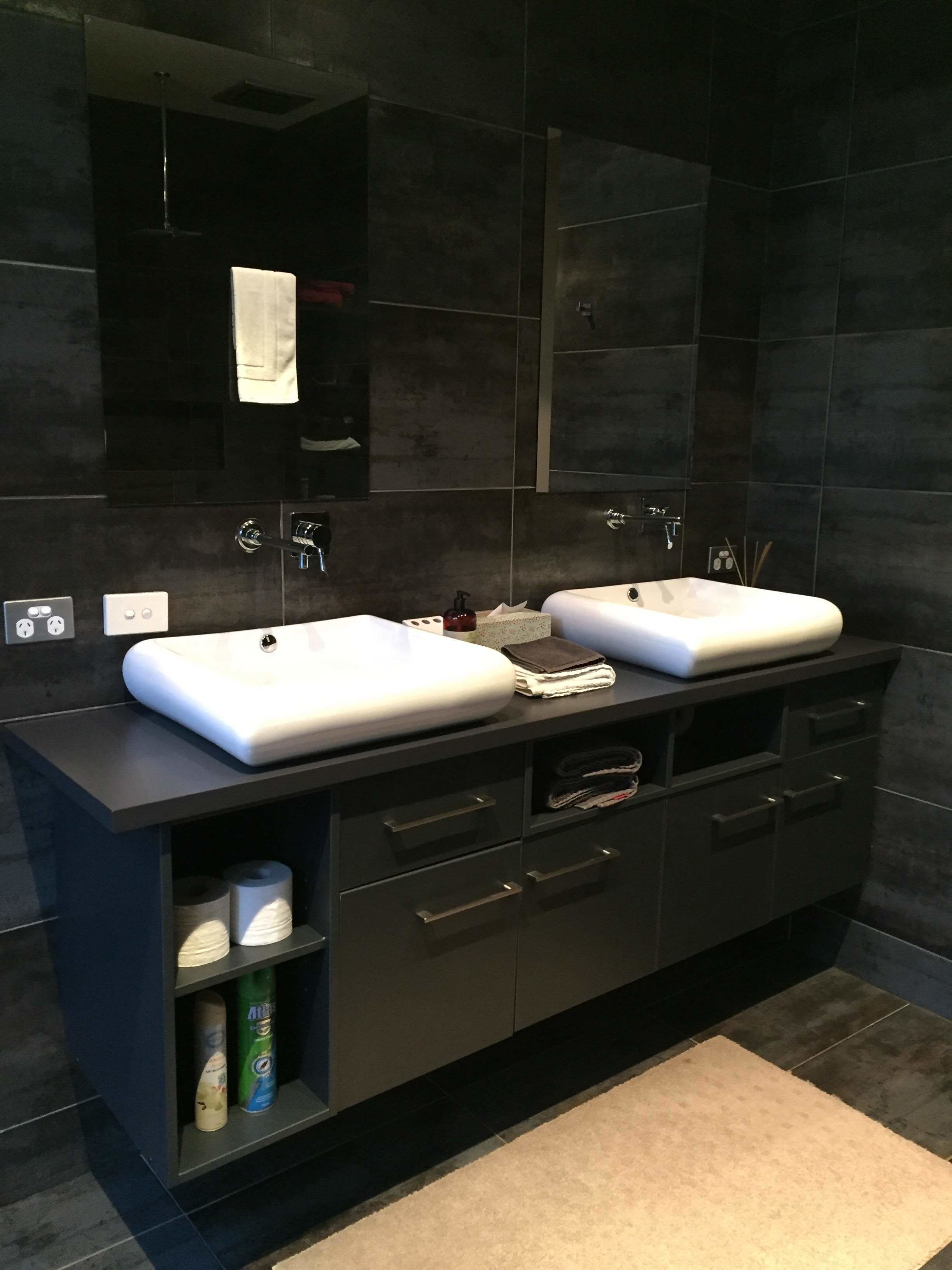 Un baño moderno con dos lavamanos, un espejo grande y un mueble de tocador de tonos oscuros con cajones y estantes.
