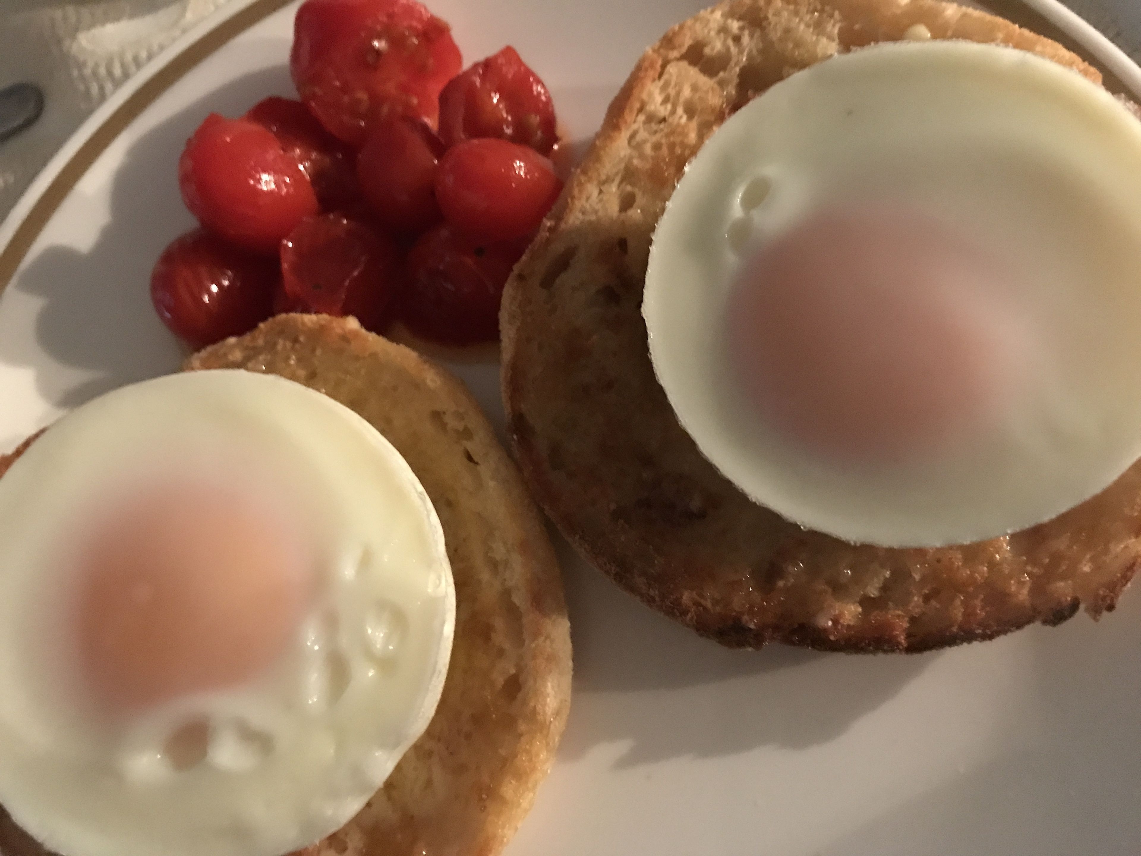 A plate with two fried eggs, a slice of toast, and cherry tomatoes.