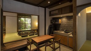 Quarto em estilo japonês tradicional, com tatames, uma mesa de jantar de madeira e uma cozinha com pia e fogão.