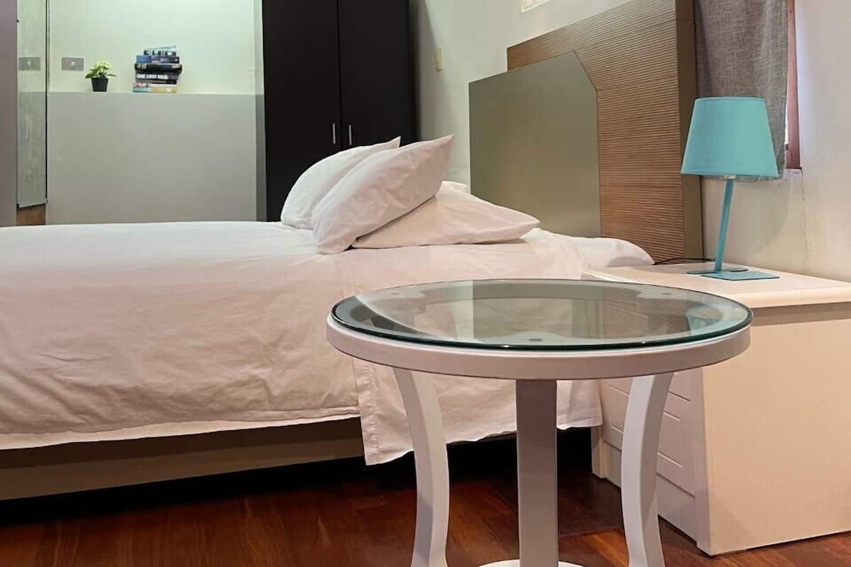 Um quarto moderno com cama, mesa de vidro, mesa de cabeceira, abajur e guarda-roupa.
