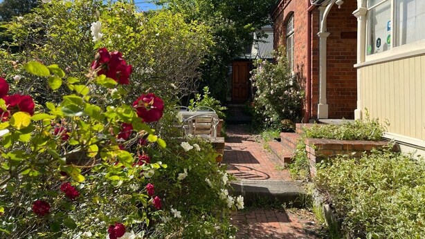 A garden pathway leading to a brick house with a white door and windows. - Lowena Cafe and Accommodation (Hobart)