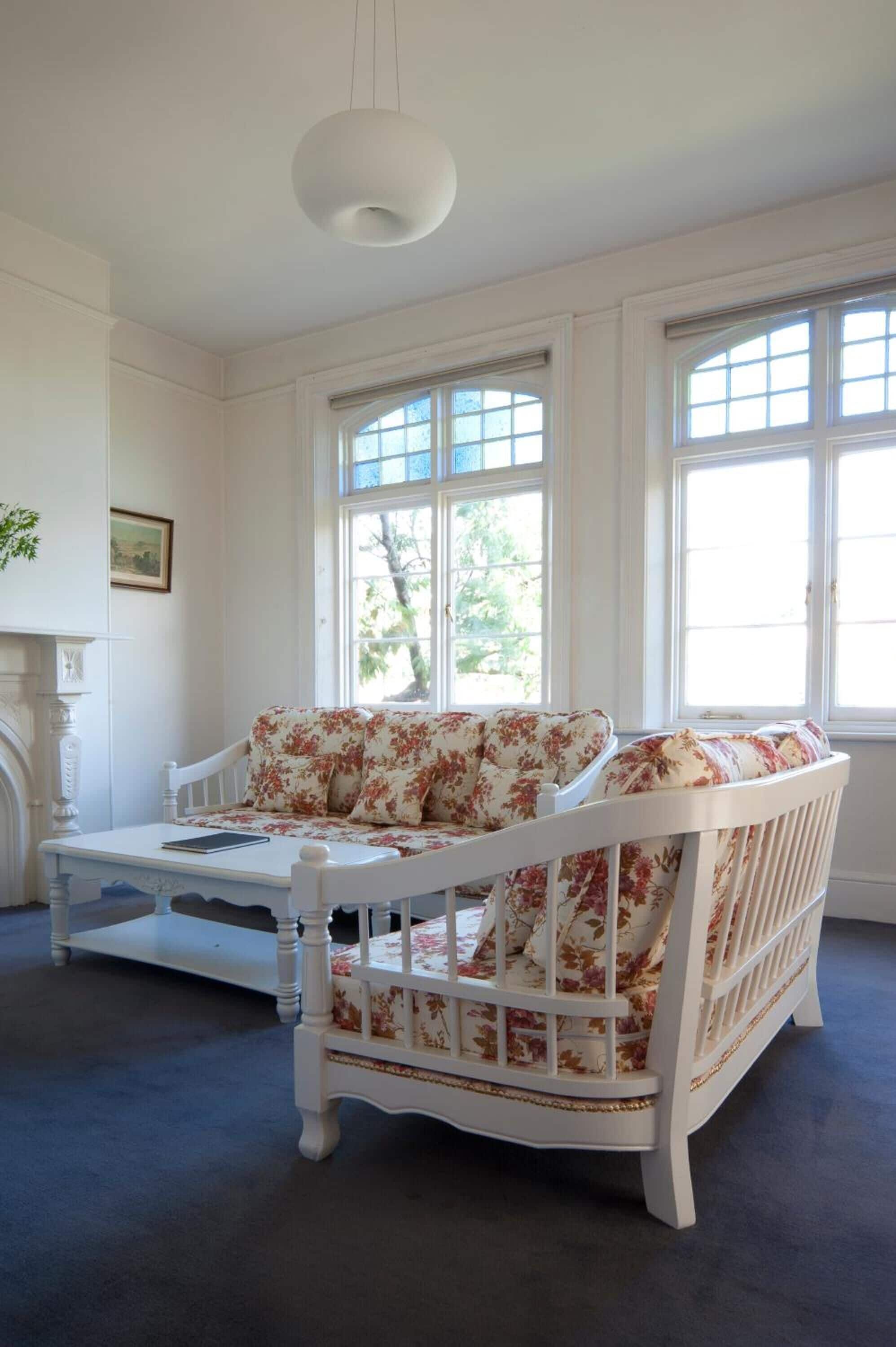 Ein weißes, floral verziertes Sofa mit passender Bank in einem hellen Raum mit großen Fenstern.