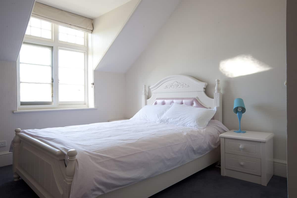 Quarto com uma cama de solteiro, mesa de cabeceira, luminária e janela.