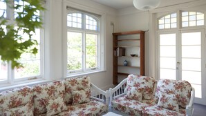 A room with two floral-patterned sofas, a wooden bookshelf, and large windows with white frames. - Lowena Cafe and Accommodation (Hobart)