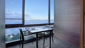 A room with a large window overlooking a body of water, a wooden table with a chair, and a carpeted floor. - Atami SEKAIE (Atami)