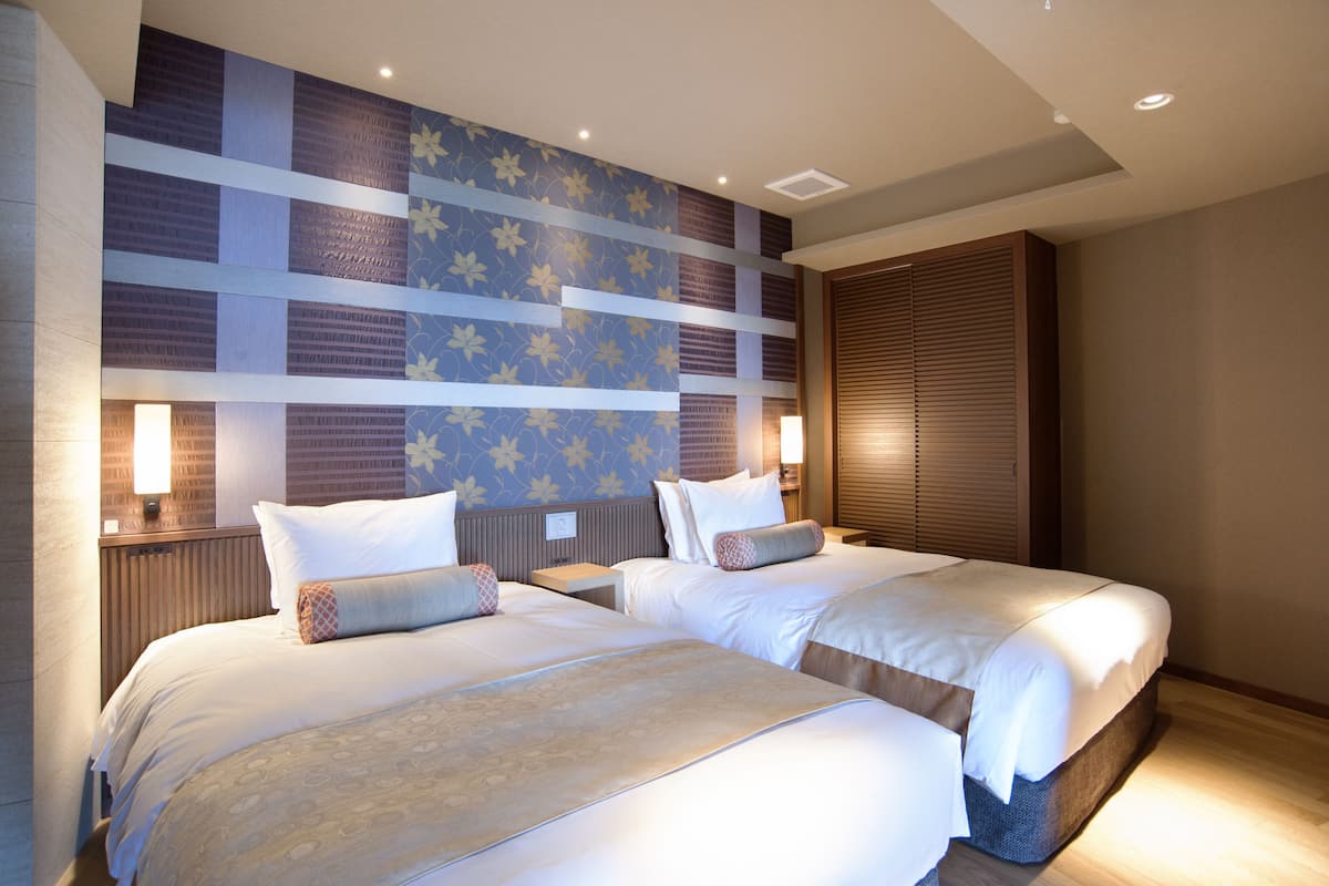 A hotel room with two beds, a patterned wall, and a wooden headboard.