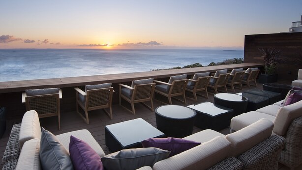 A sunlit outdoor seating area with wicker furniture and a view of the ocean at sunset. - Atami SEKAIE (Atami)