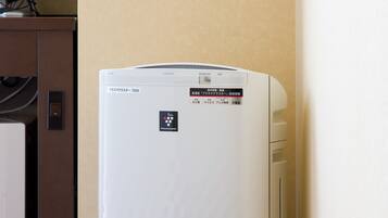 Een witte Sharp airconditioner in een hoek van een hotelkamer, met een bruin kastje en een televisie erboven.
