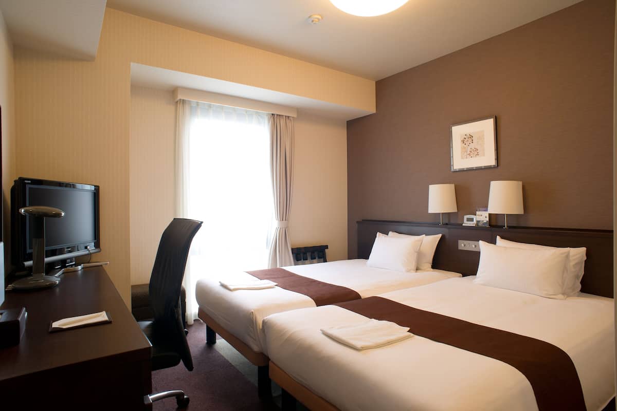 A hotel room with two beds, a desk with a television, and a window with curtains.