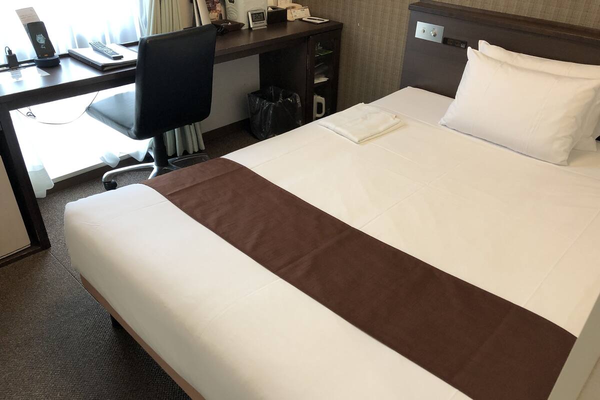 A hotel room with a bed, a desk, and a chair.