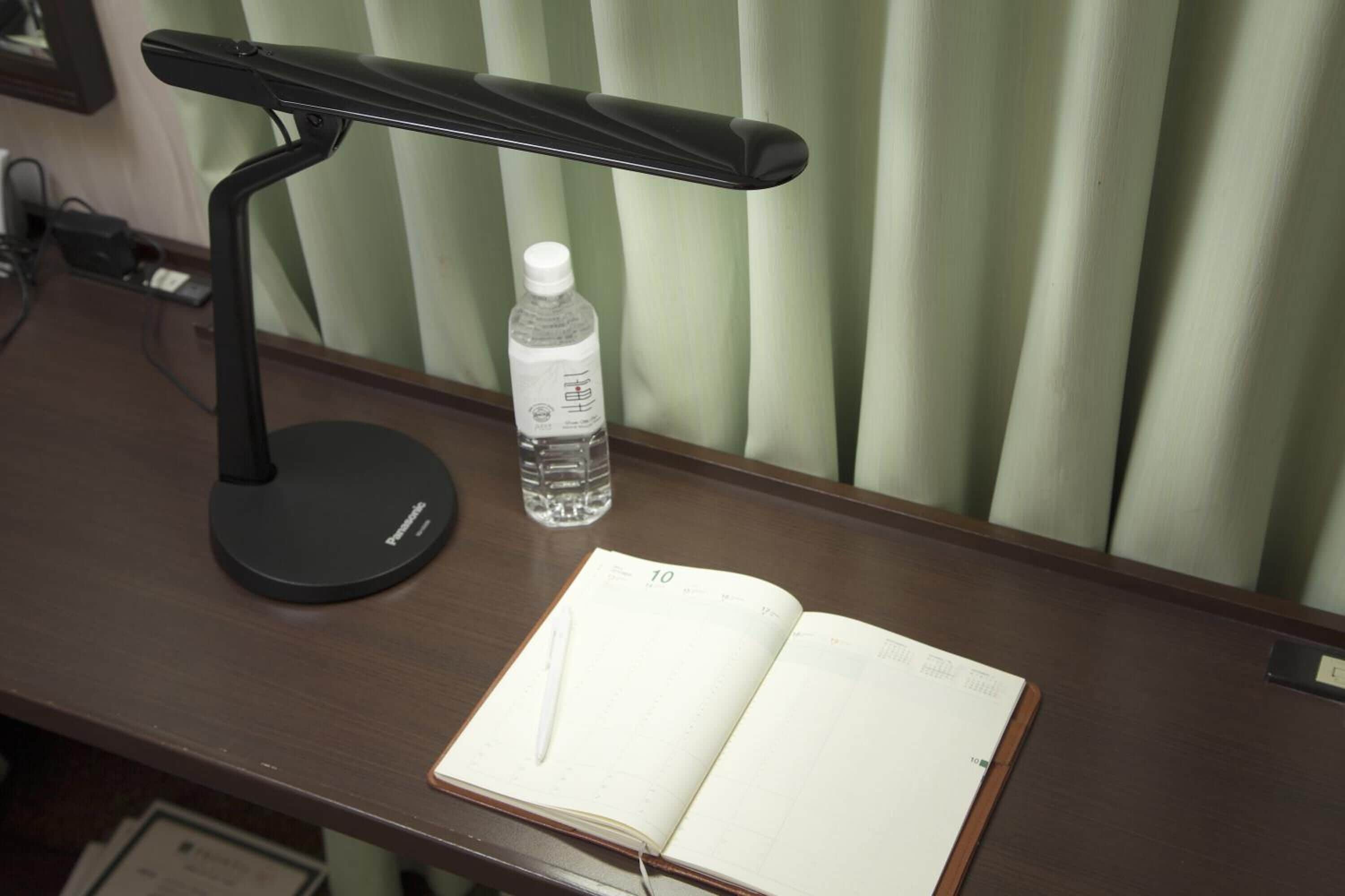 A desk with a black desk lamp, a water bottle, and an open notebook with a pen.