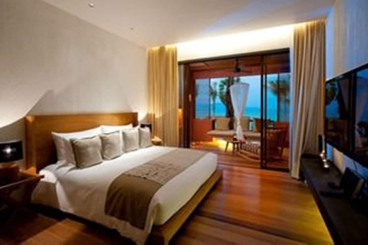A hotel room with a large bed, a TV, and a balcony with a view of the ocean.