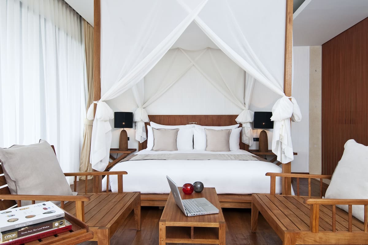 A spacious bedroom with a canopy bed, wooden furniture, and a laptop on a bedside table.