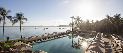 A poolside area with lounge chairs and umbrellas, overlooking a calm sea with boats.