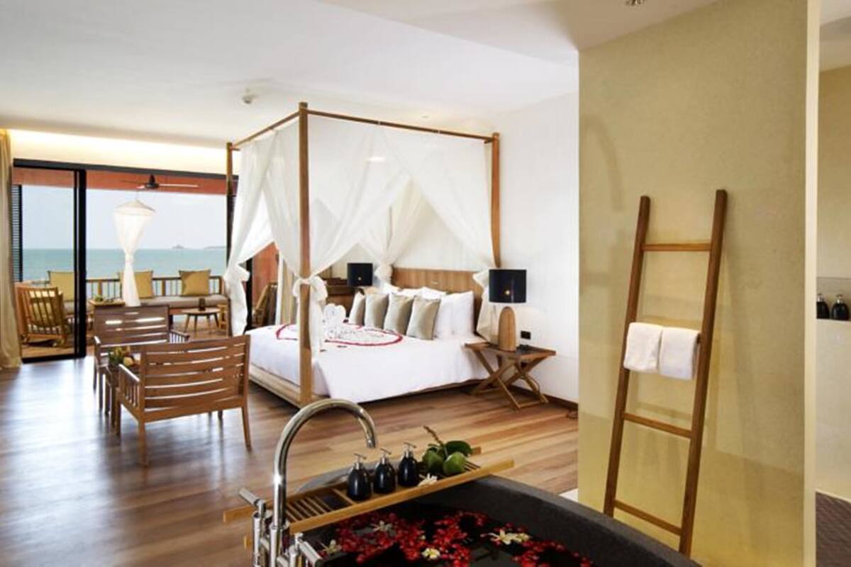 A four-poster bed with a canopy, a sitting area with a view of the sea, and a bathtub with flowers.