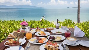 A breakfast table with various dishes, a coffee cup, and a view of the ocean and palm trees. - Hansar Samui Resort & Spa (Koh Samui)