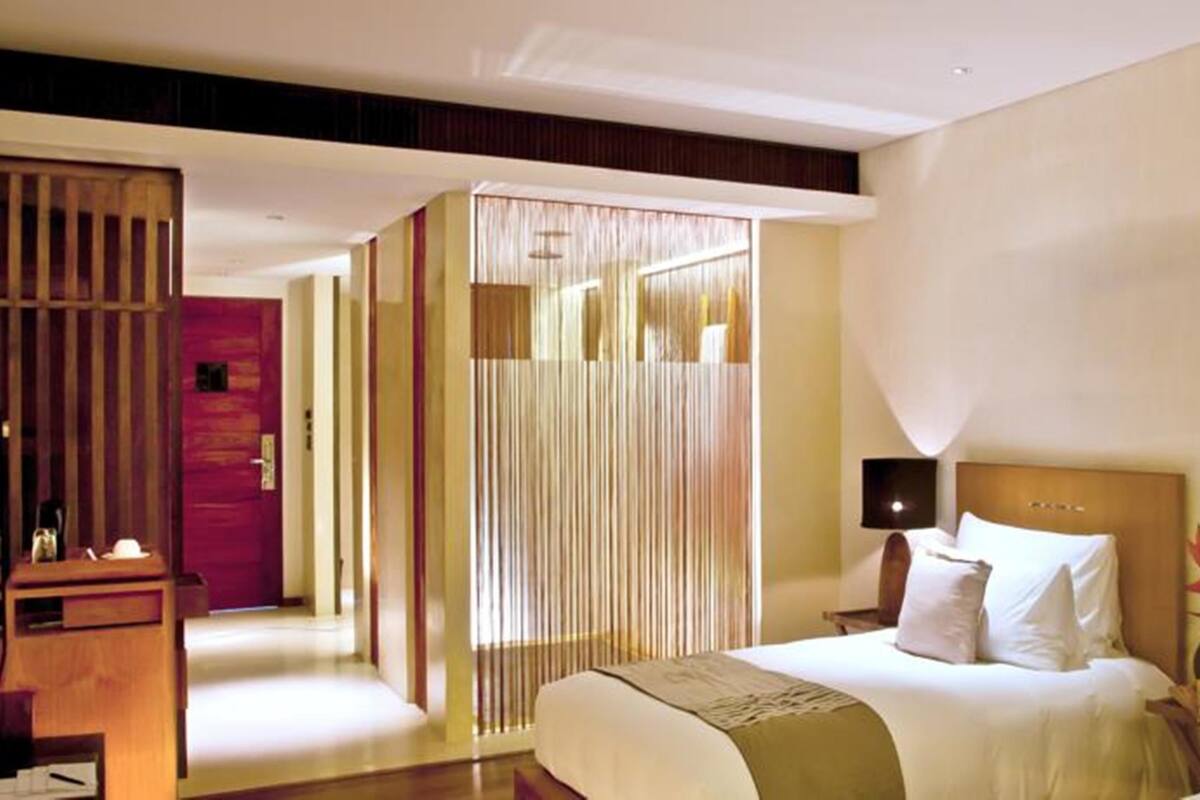 A hotel room with a large bed, a bedside table, a nightstand, and a view of a corridor.