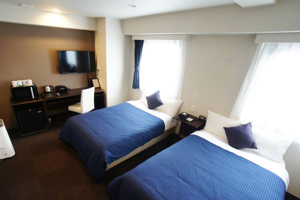 A hotel room with two beds, a TV, a desk with a computer, and a coffee maker.