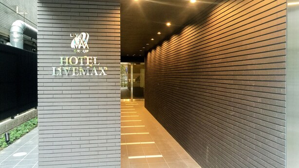 A hallway with a sign for Hotel LVMAX, featuring a modern design with brick walls and a tiled floor. - HOTEL LiVEMAX Kasai Ekimae (Tokyo)