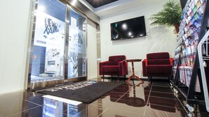 A lobby with a reception desk, two red chairs, a small table, a TV mounted on the wall, and a plant. - HOTEL LiVEMAX Kasai Ekimae (Tokyo)