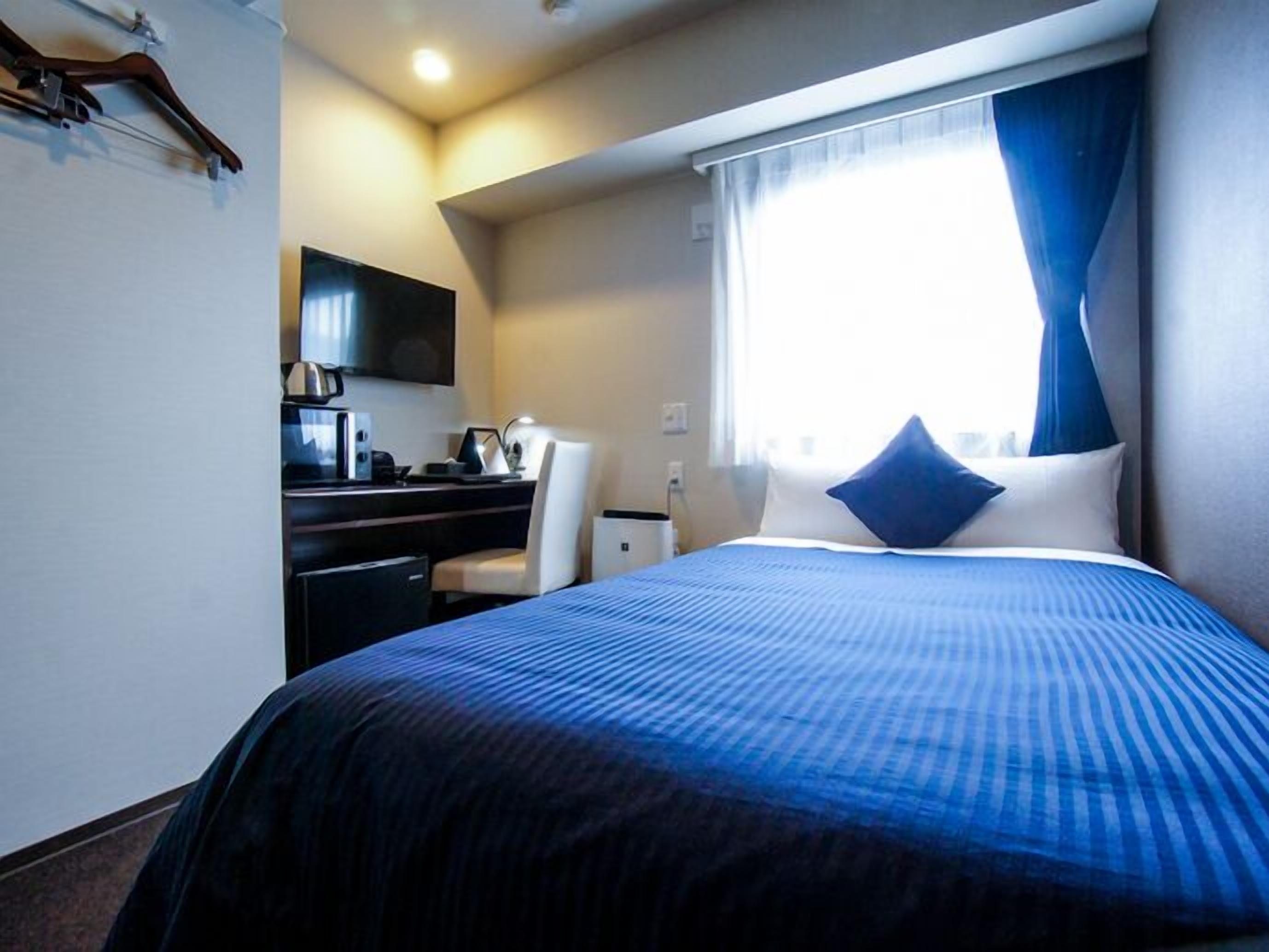 A hotel room with a bed, a desk, a chair, a television, and a window with curtains.