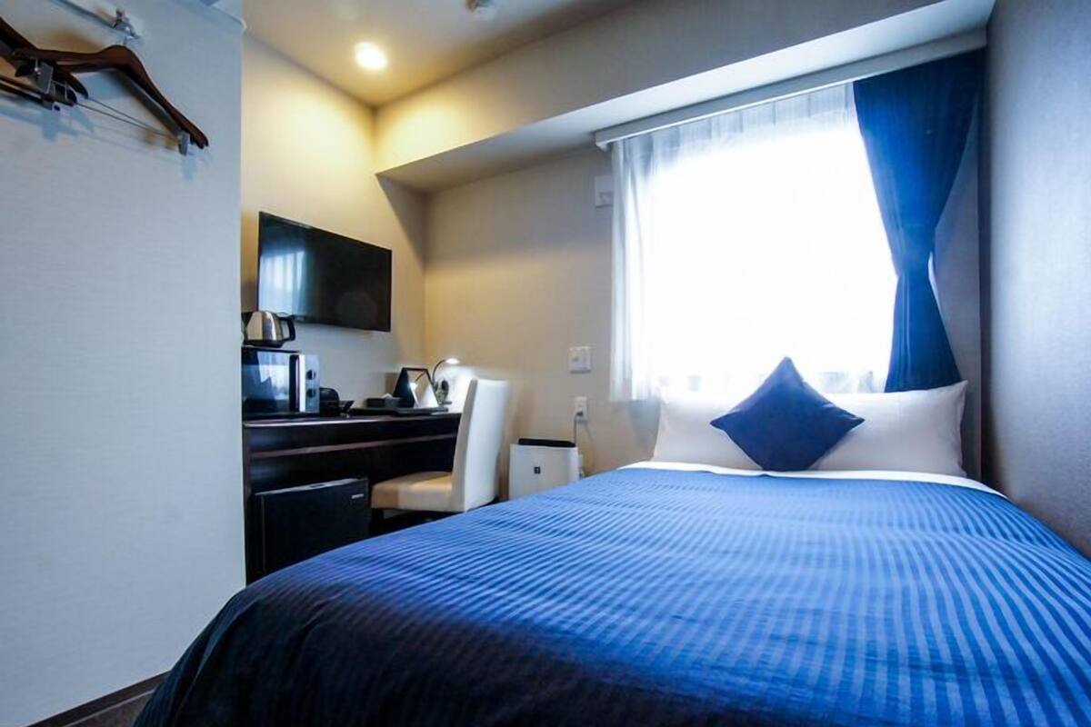 A hotel room with a bed, a desk, a chair, a television, and a window with curtains.