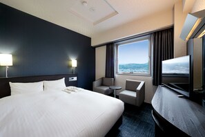 Habitación de hotel con una cama grande, un escritorio con televisor de pantalla plana, una mesita redonda pequeña, dos sillas y una ventana con vistas a las montañas.