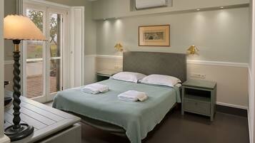 A neatly made bed with a green bedspread and two pillows, a bedside table with a lamp, and a small drawer unit.
