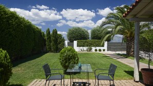A patio with a glass table and chairs, surrounded by a well-maintained lawn and various trees.