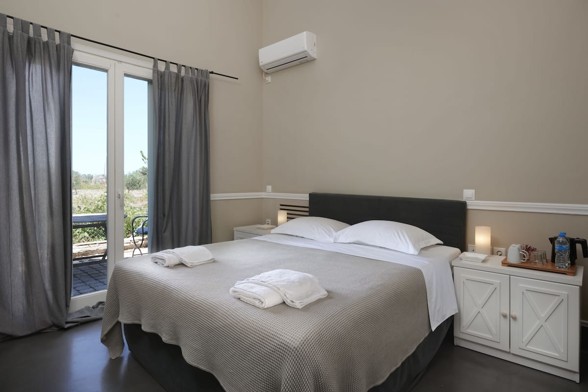 A neatly made bed with white linens, a bedside table with a lamp, and a view through a sliding door to an outdoor area.