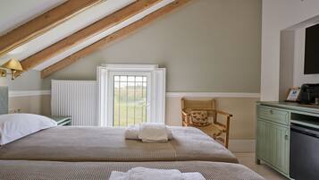 A bedroom with a sloped ceiling, a bed with a checkered bedspread, a wicker chair, a green dresser, and a radiator.