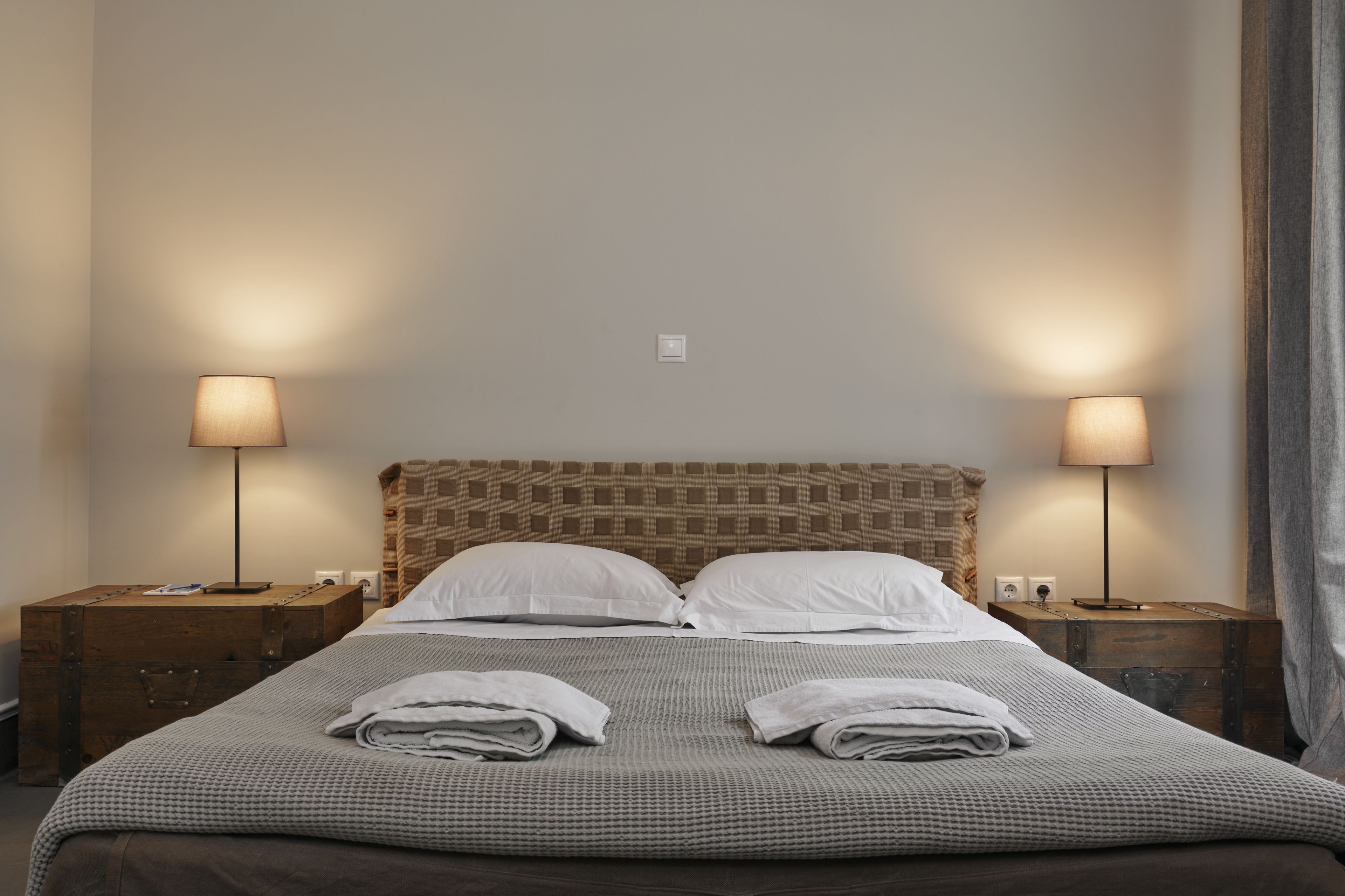 Una cama bien tendida con dos almohadas, dos mesitas de noche con lámparas, y un cabecero con estampado a cuadros.