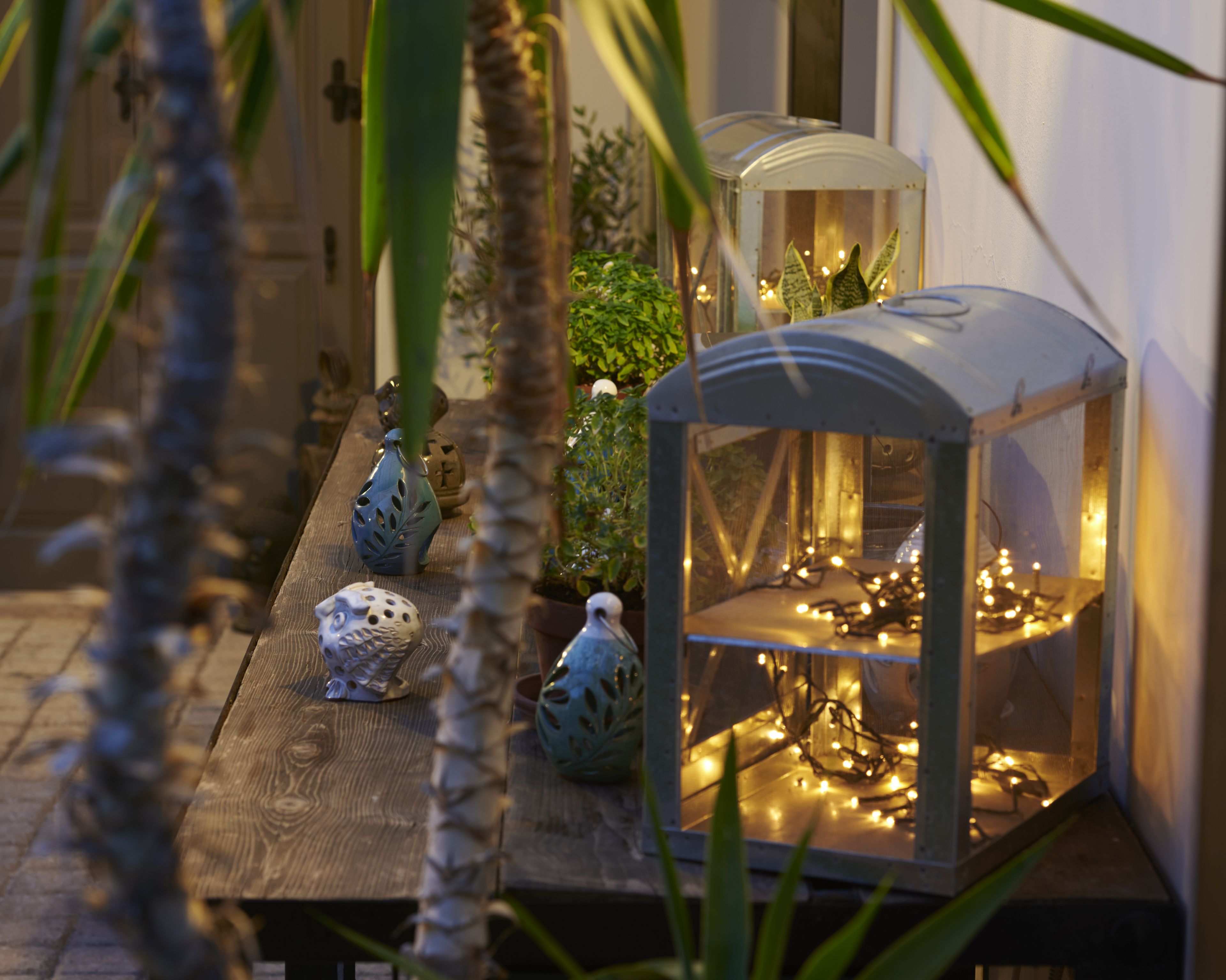 A wooden table with decorative vases, a glass terrarium with string lights, and a potted plant.
