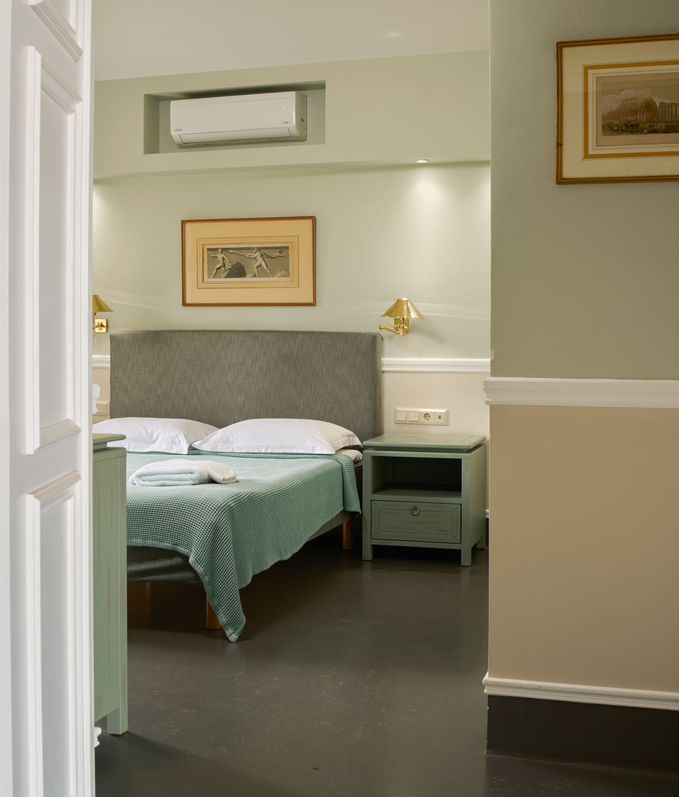 Quarto com cama, mesas de cabeceira, luminária, ar condicionado e quadro pendurado na parede.