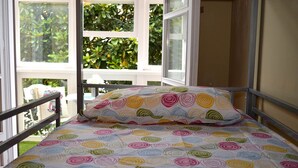 A bed with a colorful circular pattern bedspread and matching pillow, positioned in a room with large windows and a view of greenery outside. - Hostel Santander (Santander)