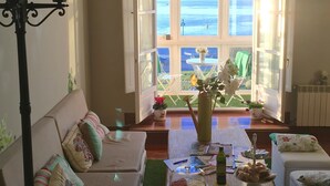 A cozy living room with a sofa, a coffee table with snacks, and a view of the sea through open windows. - Hostel Santander (Santander)