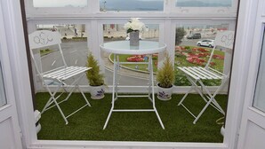 A balcony with two white folding chairs, a small table with a vase of flowers, and potted plants. - Hostel Santander (Santander)