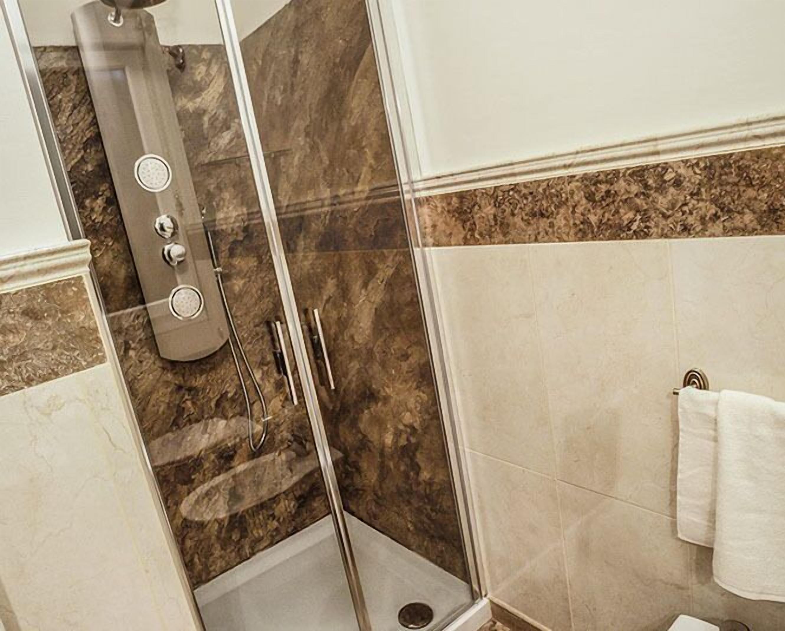 A shower with a glass door, a handheld showerhead, and a handheld scrubber.