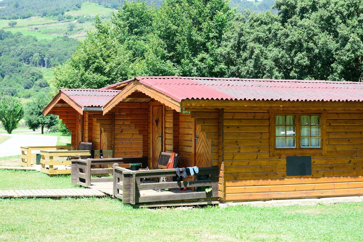 A row of wooden cabins with a red roof, each with a porch and a bench.